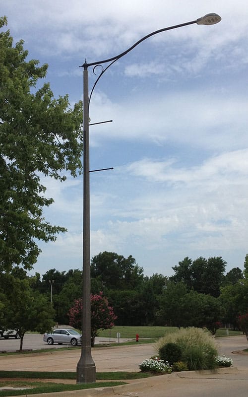 Light fixture accompanied by banner arms and a scroll style arm all on a Centennial pole.