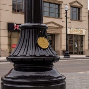 A KSB16 Florentine Sr. decorative split base accompanied by a custom 'Oakville' emblem on a fluted pole. This project is on one of the busy streets of Oakville, Ontario.
