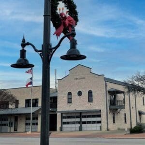 K807 Doral Sr. and K707 Doral Jr. pendants accompanied by a KA30 scroll arm with decorative scroll, two KA40 mini scroll arms with decorative scrolls, and banner arms atop a Washington style pole. This project is in Fredericksburg, Texas during Christmas time.