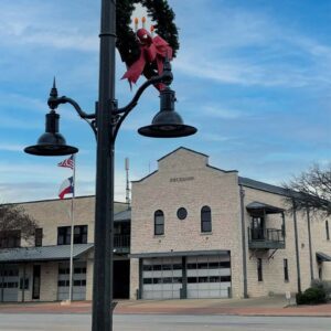 K807 Doral Sr. and K707 Doral Jr. pendants accompanied by a KA30 scroll arm with decorative scroll, two KA40 mini scroll arms with decorative scrolls, and banner arms atop a Washington style pole. This project is in Fredericksburg, Texas during Christmas time.