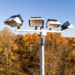 An assembled Spartan Sports Lighting project including KSL1 fixtures and a cross arm atop a sports lighting pole. This project is overlooking a sports field and is surrounded by orange/gold trees.